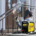 Hombre soldando un barandal metálico afuera de una casa con la Soldadora Inversora KMA160 Kerher