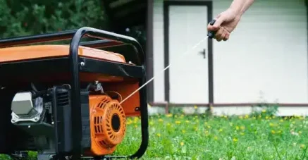 Profesional encendiendo un generador naranja durante tareas de mantenimiento de generadores en exteriores.